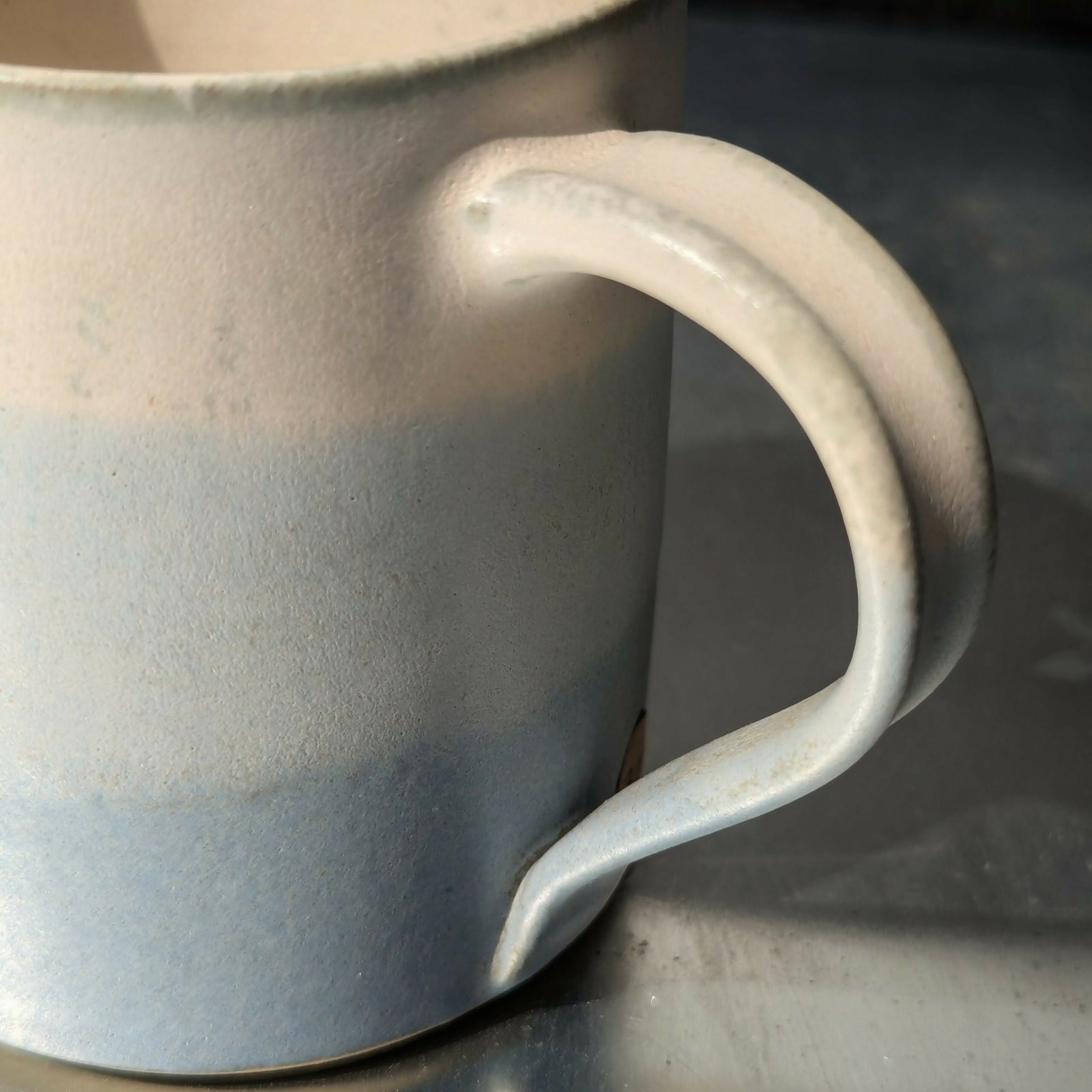 Un mug en grès blanc, tourné et ansé à la main, et émaillé en dégradé de bleu et blanc.