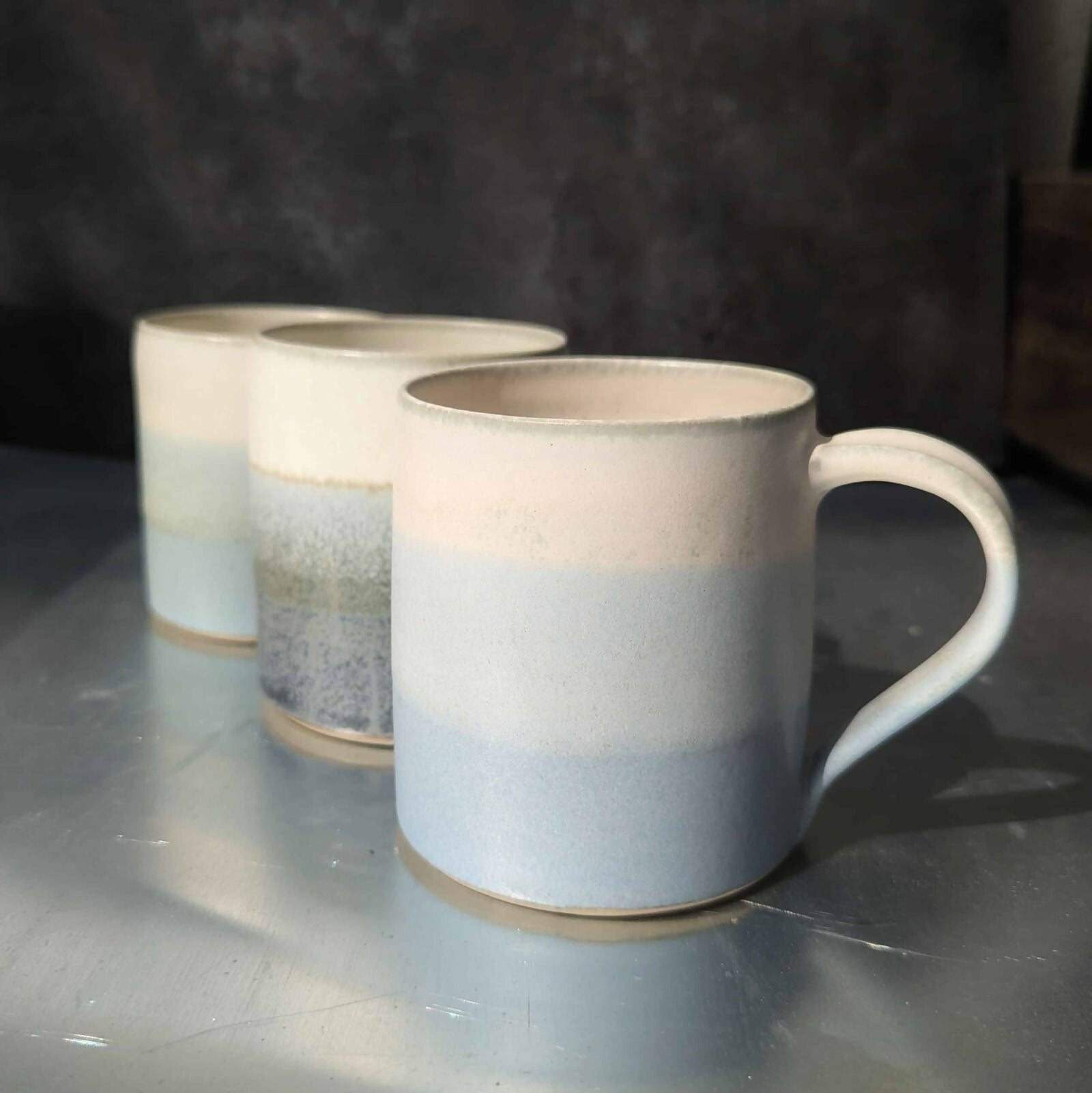 Un mug en grès blanc, tourné et ansé à la main, et émaillé en dégradé de bleu et blanc.