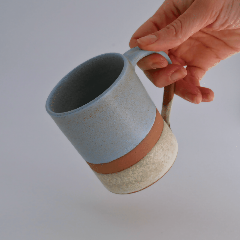 Mug en grès rouge, émaillé bleu sur la partie supérieure et blanc sur la partie inférieure, avec une bande de séparation non émaillée laissant la terre apparente.