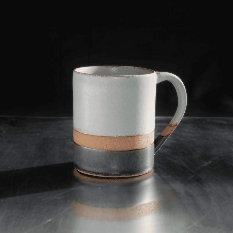 Mug en grès rouge, émaillé vert d'eau sur la partie supérieure et noir sur la partie inférieure, avec une bande de séparation non émaillée laissant la terre apparente. Présenté debout sur une surface refléchissante et fond noir.